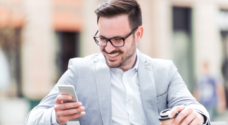 Homem de óculos e terno sorrindo e olhando para o celular.