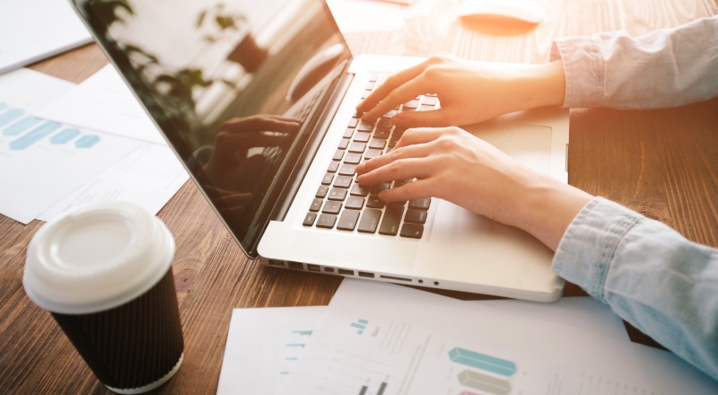 Homem usando notebook em uma mesa com documentos contendo gráficos de barras 