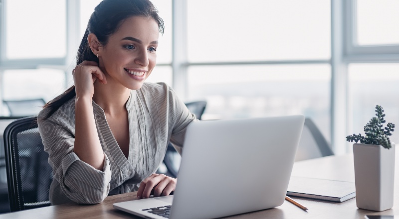Mulher branca sorrindo de frente para o computador, pois o site que ela está carrega rápido por usar técnicas de Lazy Loading