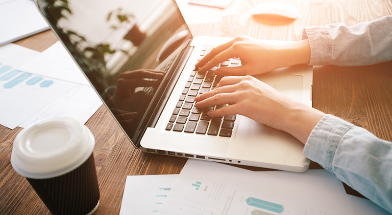 Homem mexendo em um notebook com um copo de café ao lado