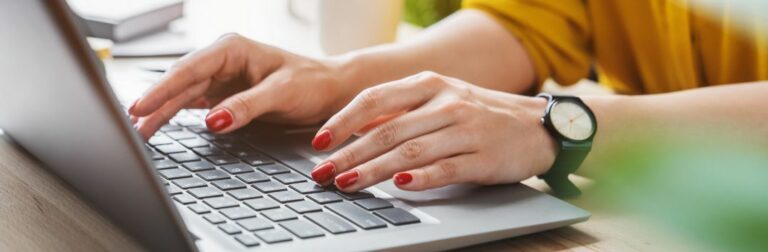 mãos com unhas pintadas de vermelho digitando em um notebook