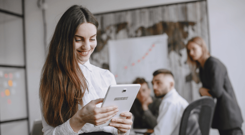 Mulher branca sorridente olhando um tablet.