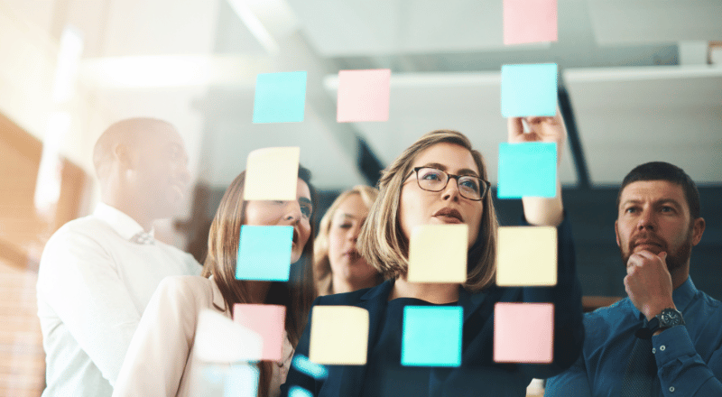 Equipe criando estratégias de marketing de conteúdo através de post-its em uma lousa transparente.