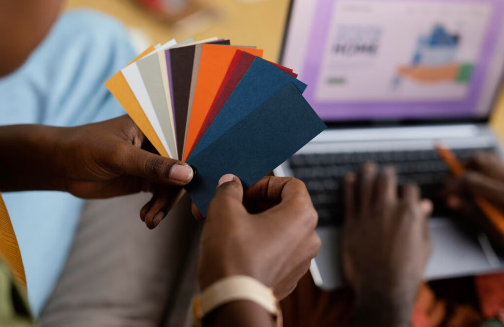 Mãos negras segruando diversos cards com diversas cores cada um em frente a um notebook