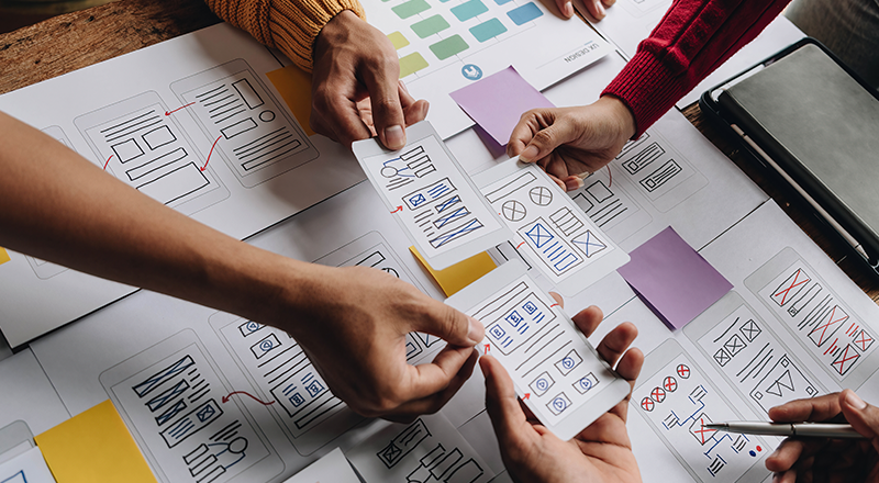 Diversas mãos trabalhando em uma mesa com diversos papéis de sitemap.