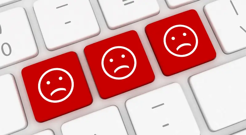 Imagem mostra um teclado de computador, com teclas brancas, focando em três vermelhas om smiles tristes desenhados nelas.