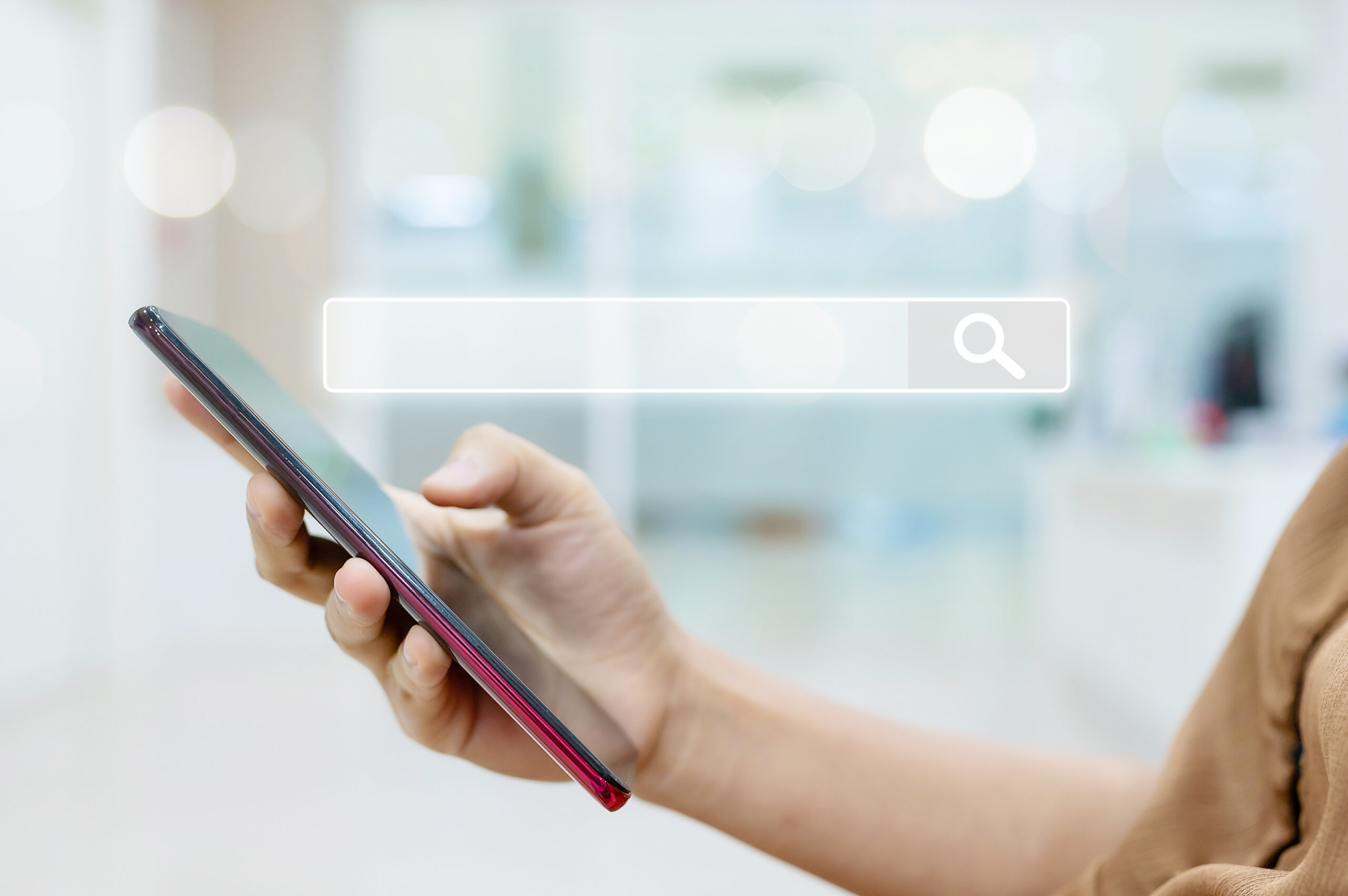 Entity SEO: Conheça esta estratégia ideal para o seu conteúdo Mão de uma pessoa mexendo em um smasrtphone e uma barra de campo de busca translucida em cima