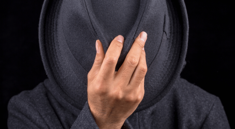 Cloaking: o que é e qual o impacto no SEO? Homem retirando chapéu preto do rosto, simbolizando um cloaking SEO