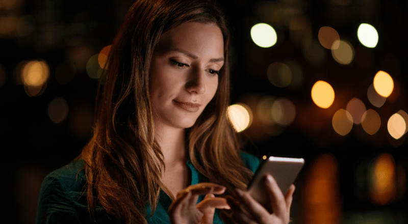 Rolagem infinita: Veja como melhorar o SEO do seu site Mulher branca observando a tela do celular e realizando a rolagem infinita.