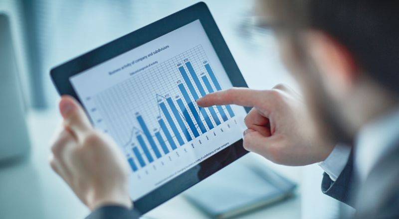 Planejamento Estratégico: Como fazer dicas e exemplos Homem de terno, analisando um gráfico de colunas que está aparecendo na tela de um tablet.
