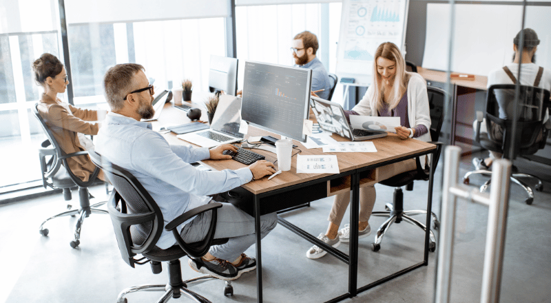 Inteligência Artificial e SEO: Impulsione a visibilidade do seu site no Google Ilha de computadores com quatro computadores e quatro pessoas todas trabalhando para unir inteligência artificial e SEO.