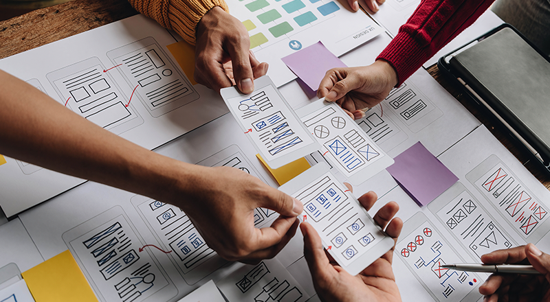 O que é um sitemap e como utilizá-lo para melhorar o SEO do seu site? Diversas mãos trabalhando em uma mesa com diversos papéis de sitemap.