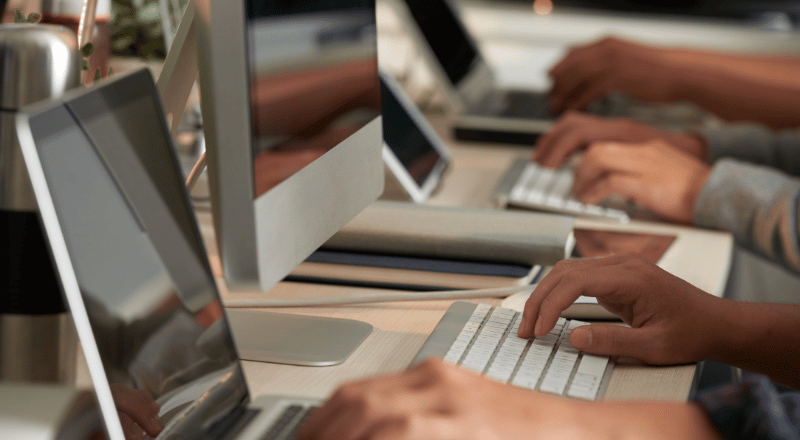 Por que a Acessibilidade digital é importante para o sucesso do seu site Imagem mostra mãos de algumas pessoas mexendo em computadores, uma ao lado da outra.