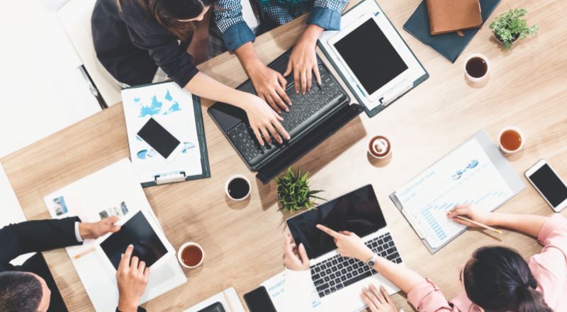 Menção de marca: qual o verdadeiro impacto para o SEO do seu site Mesa de trabalho rodeada de pessoas discutindo estratégias de mensão de marca.