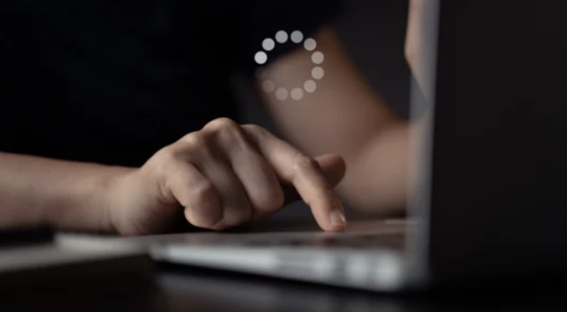 Lazy Loading: saiba o que é e a sua importância Pessoa mexendo no notebook e o sinal de carregando página no centro da imagem mostrando que é uma boa ideia implemetnar o Lazy Loading