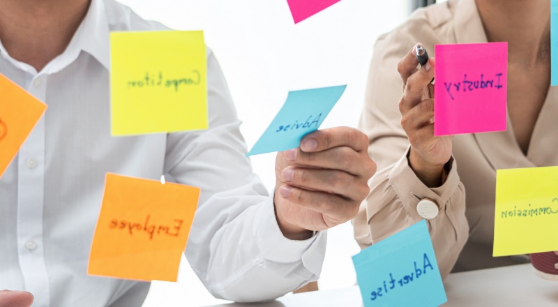 A importância das Branded Keywords para a Estratégia de SEO Duas pessoas pegando e analisando postites coloridos e escritos